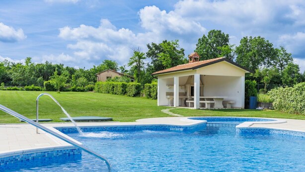 A swimming pool with a small pavilion and a grassy area in the background. - Nice apartment for 8 guests with A/C, WIFI, pool, TV and terrace (Pazin)