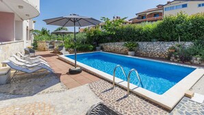 Une piscine entourée de murs de pierre et de verdure, avec des chaises longues et des parasols.
