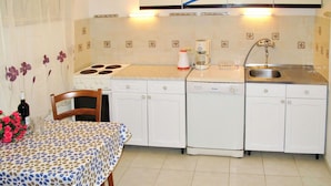 A compact kitchen with a stove, sink, and dishwasher. There is a dining table with a patterned tablecloth and a chair. - Beautiful apartment for 3 guests with WIFI, A/C, TV, terrace and pets allowed (Rovinj)