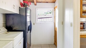 Cucina piccola e stretta con un frigorifero nero, una finestra vista sul verde e un soffitto in legno.