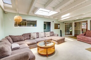 A spacious living room with a sectional sofa, a round coffee table, and a large window providing natural light. - Walk to the Beach! Spacious 6BR La Jolla Home (La Jolla)