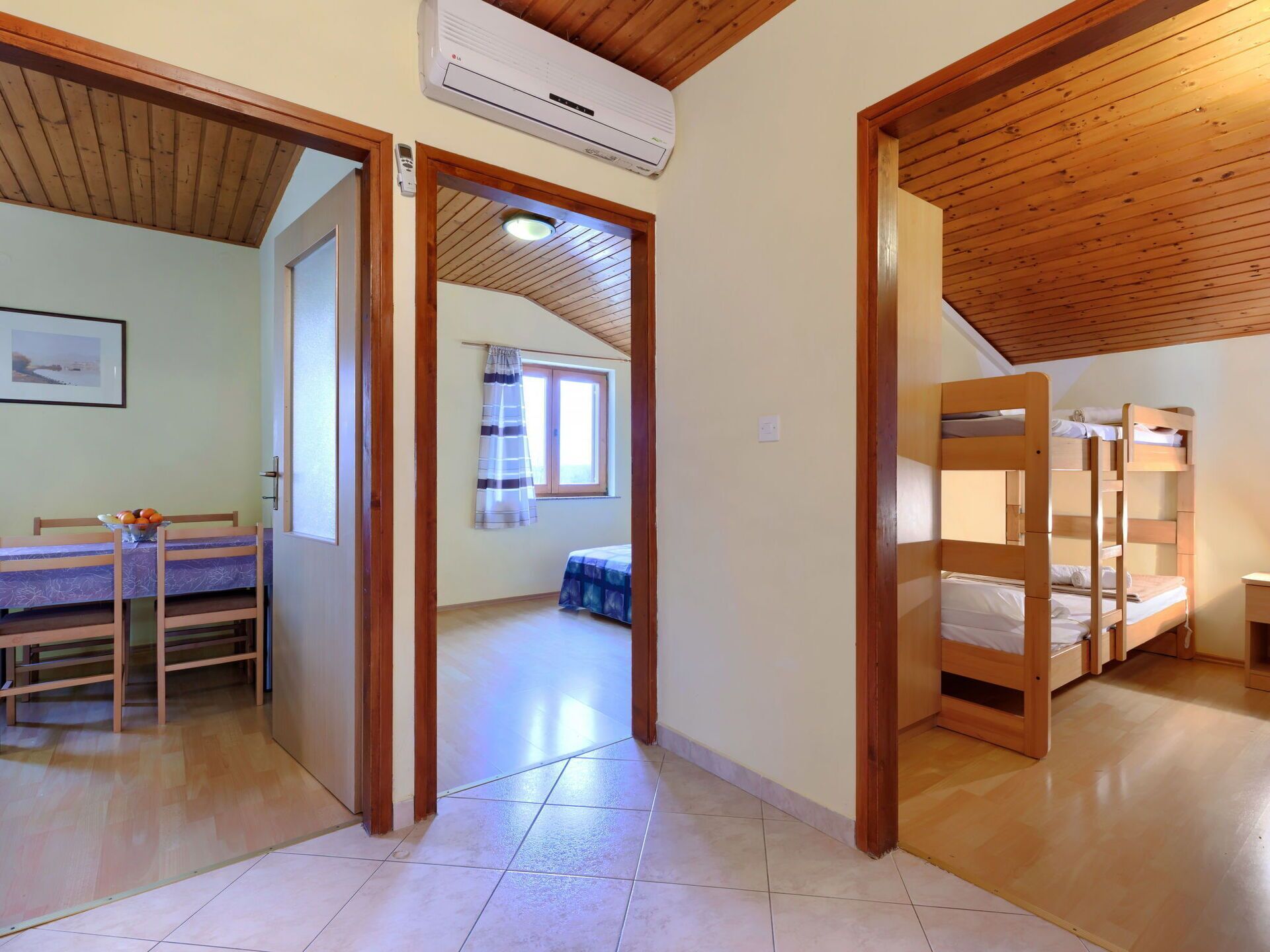 A room with a wooden ceiling, a bunk bed, a desk with a chair, and a window with curtains.