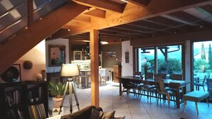 A spacious loft with a high ceiling, exposed wooden beams, a dining area with a view, and a cozy seating area with a lamp.