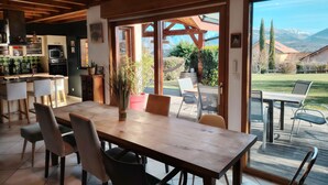 Une cuisine moderne dotée d’appareils électroménagers intégrés, un coin repas avec une table et des chaises en bois, et une vue sur un paysage montagneux grâce à de grandes portes-fenêtres coulissantes.