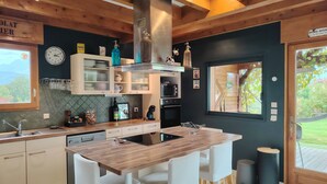 Une cuisine moderne avec un îlot en bois, des chaises blanches et une vue sur l’extérieur grâce à une fenêtre.