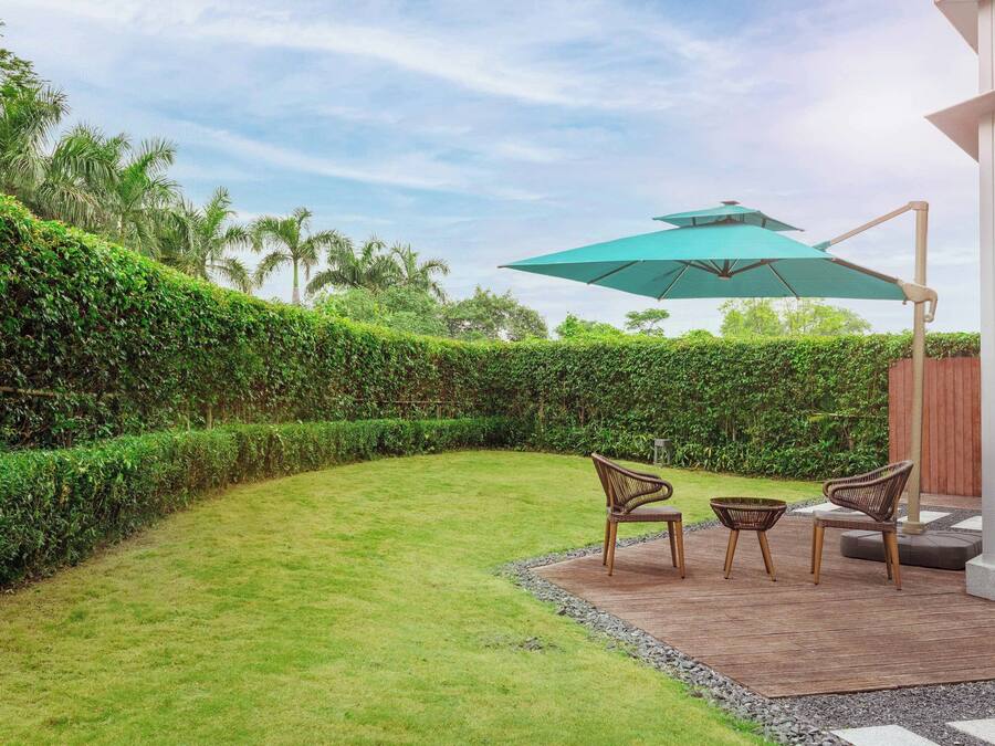 A landscaped outdoor area with a wooden deck, two wicker chairs, and a large umbrella.