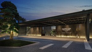 A modern building with a covered entrance, a tree in the foreground, and illuminated signage.