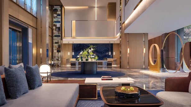 A spacious lobby with a central round table, seating areas, and a staircase.
