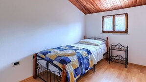 A single bed with a wooden headboard, a window with curtains, and a wooden ceiling.