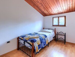 A single bed with a wooden headboard, a window with curtains, and a wooden ceiling.