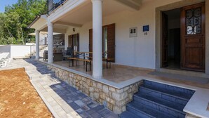 A covered outdoor area with stone steps leading to a wooden door, a bench, and a table with chairs.