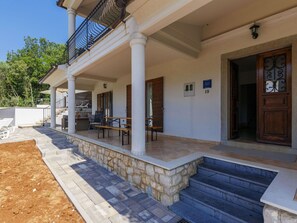 A covered outdoor area with stone steps leading to a wooden door, a bench, and a table with chairs.