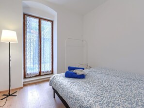 Quarto com cama, janela com cortinas, luminária de chão e mesa de cabeceira.