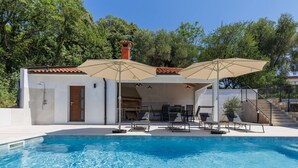 A swimming pool with lounge chairs and umbrellas, a covered patio area, and a stone staircase.