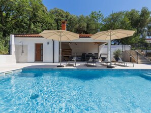 A swimming pool with lounge chairs and umbrellas, a covered patio area, and a stone staircase.