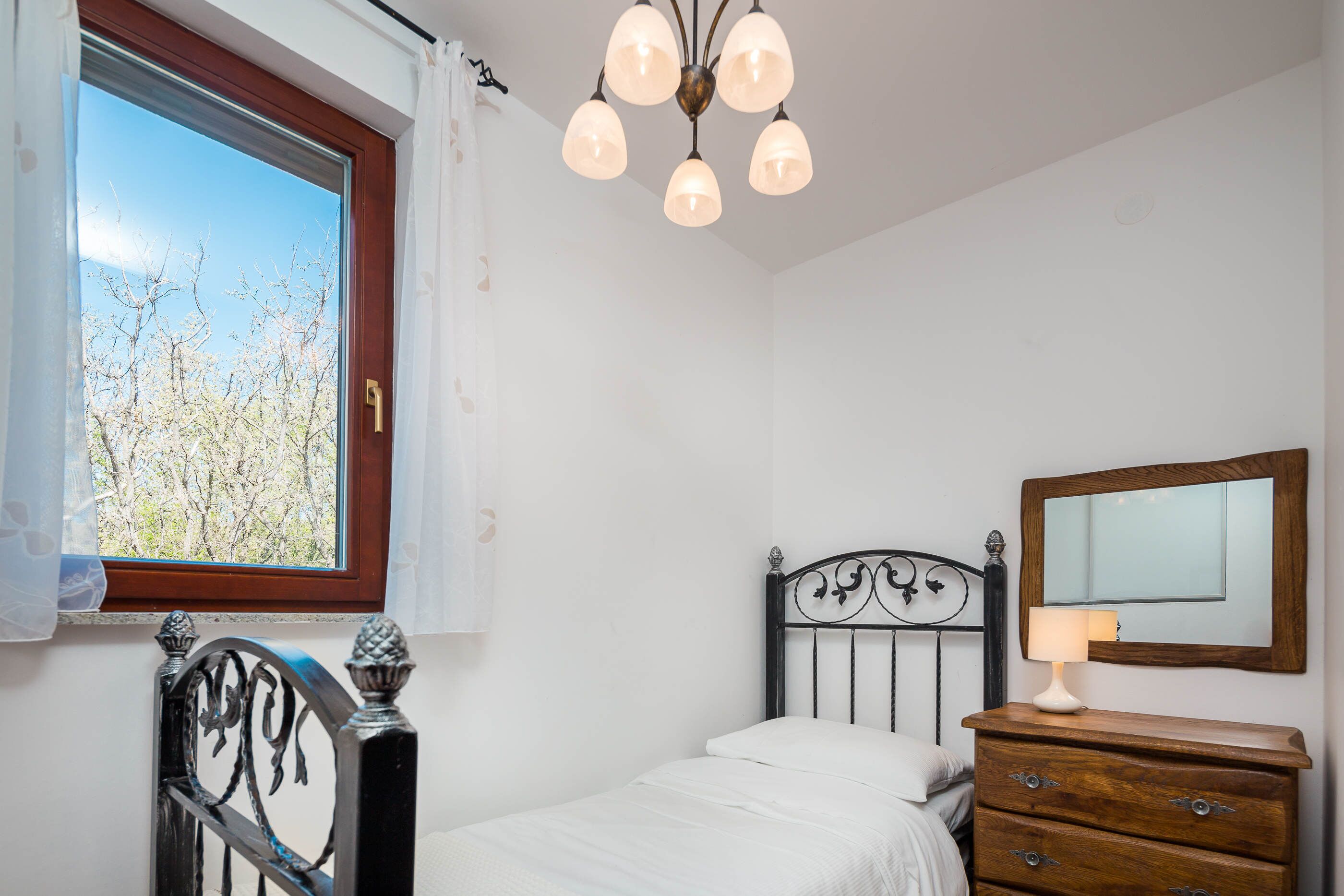 A bedroom with a bed, a dresser, a mirror, and a window with a view of trees.