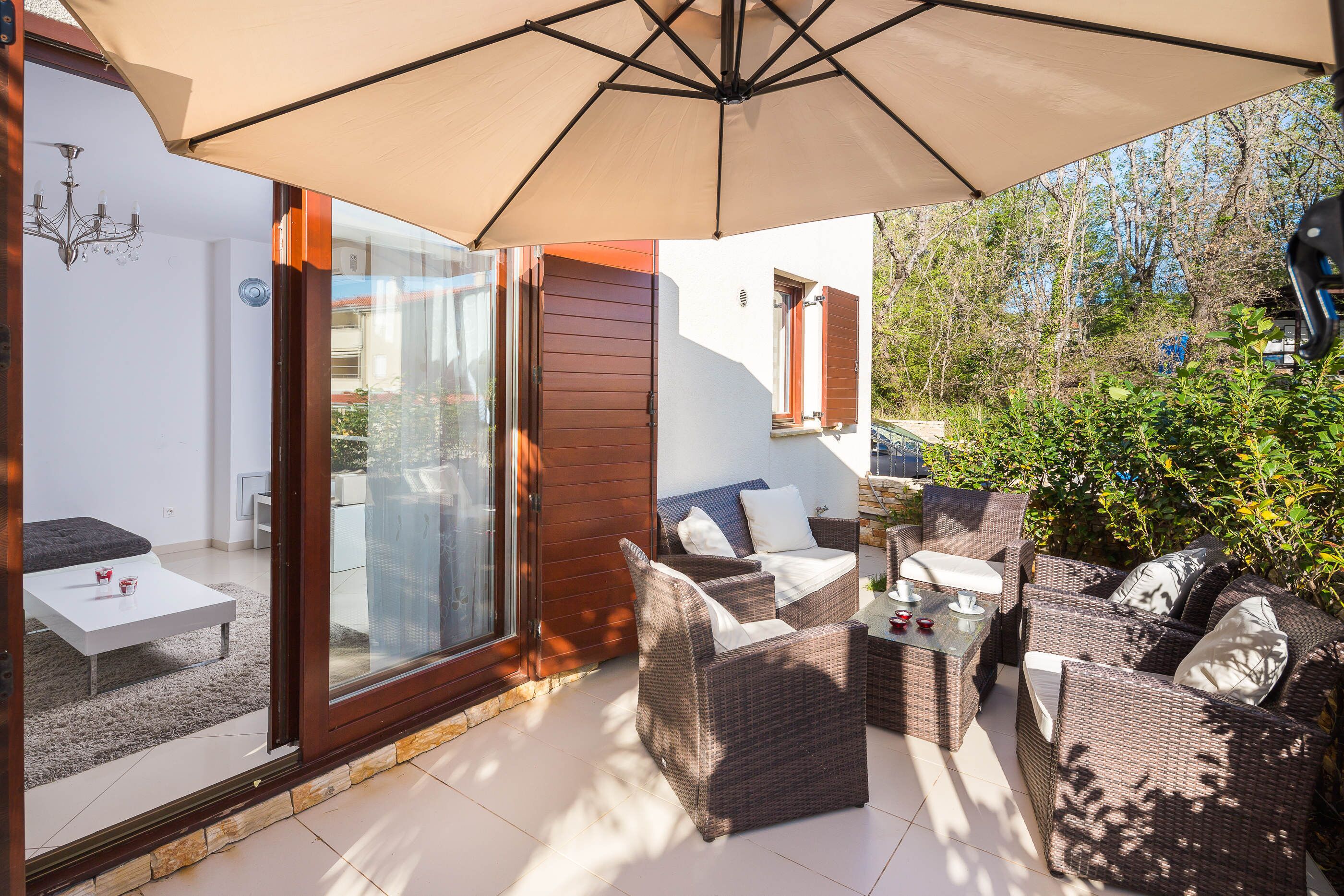 Ein Terrassenbereich mit Korbmöbeln, einem Tisch und einem großen Sonnenschirm.