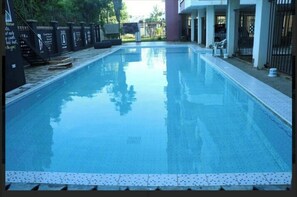 A rectangular swimming pool with a tiled edge, surrounded by a fence and a building with a covered patio area. - Hosted   by     Orah (Nyali)