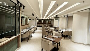 Un restaurante moderno con un área de comedor central, varias mesas y una zona de bar con una pared divisoria de vidrio.