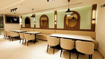 A modern restaurant with multiple tables and chairs, a long bench, and wall-mounted mirrors.