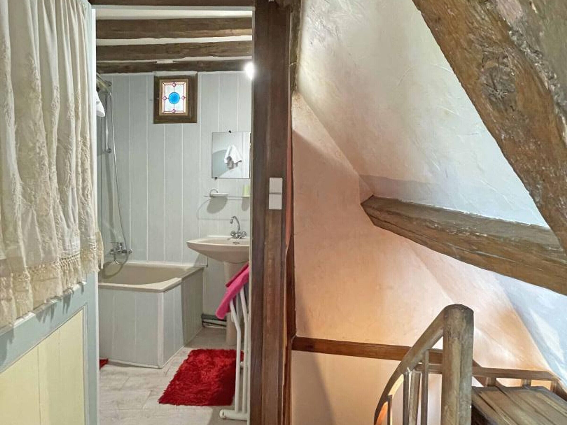 A narrow, rustic bathroom with a bathtub, sink, and a small window.