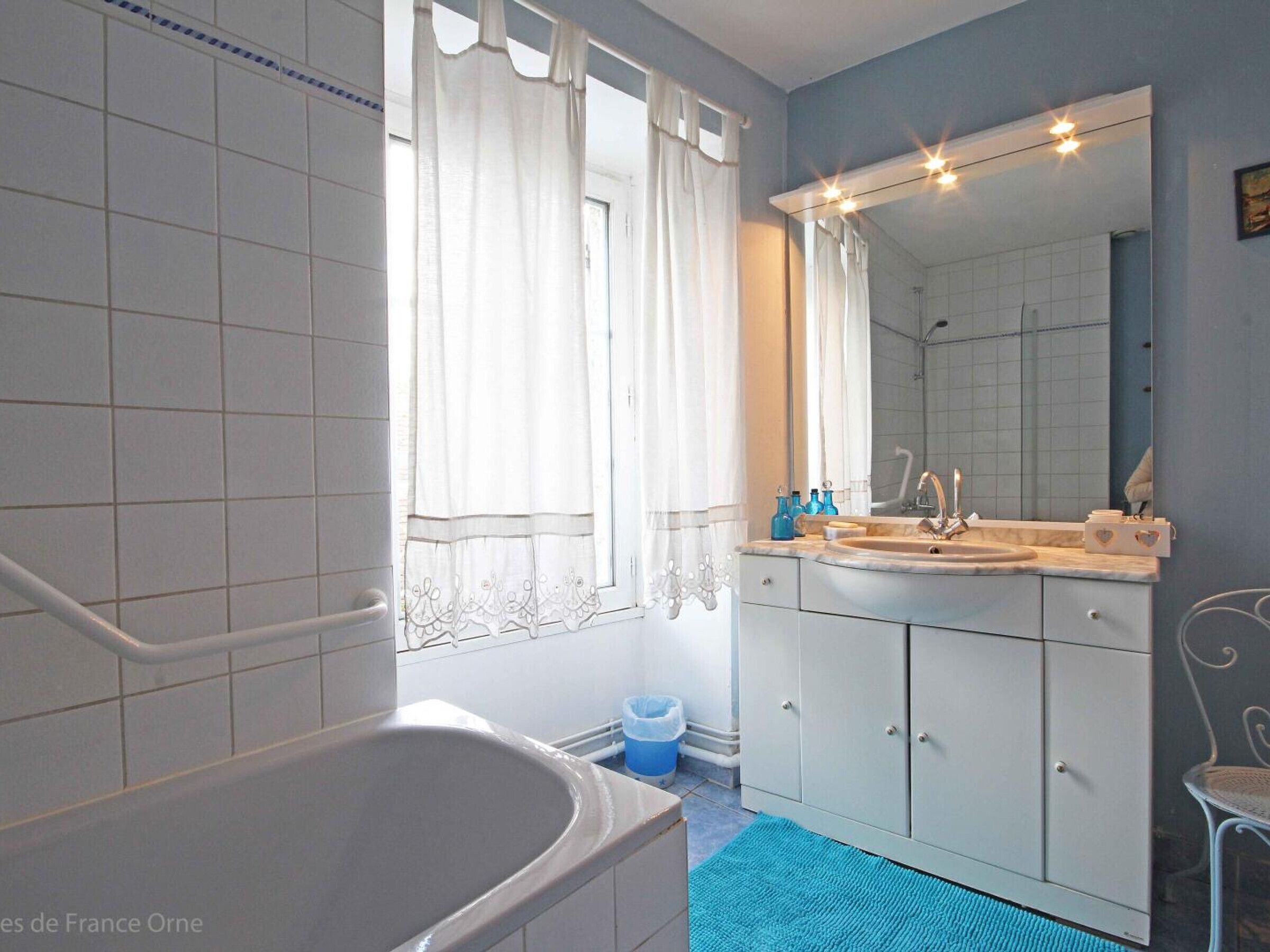 Een badkamer met een bad, een wastafel, een spiegel en een raam met gordijnen.