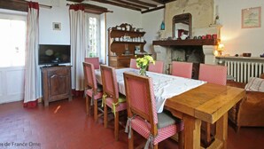 A dining area with a wooden table and chairs, a television, and a fireplace. - Cozy house near Argentan - 9 guests (Sarceaux)