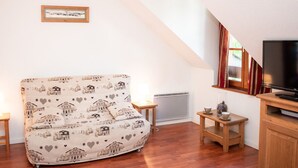 A cozy room with a sofa, a television, a small table, and a window with curtains. - Duplex 2 Rooms for 4 People with Balcony in Vignec (Vignec)