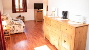 A cozy room with a bed, a TV, a wooden dresser, and a window with curtains. - Duplex 2 Rooms for 4 People with Balcony in Vignec (Vignec)