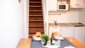 A compact kitchen with a microwave, stove, and dishwasher. A dining table is set with plates, glasses, and a bottle. - Duplex 2 Rooms for 4 People with Balcony in Vignec (Vignec)