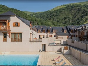 A hotel with a swimming pool, multiple balconies, and a view of green hills.
