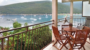 A balcony with wooden chairs and a table, overlooking a marina with boats and a hilly landscape. - Beautiful apartment for 4 guests with A/C, WIFI, TV and balcony (Labin)