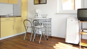 A compact kitchen with yellow cabinets, a small dining table with chairs, a coffee maker, a framed certificate, a window with blinds, and a white refrigerator. - Cosy apartment for 2 guests with WIFI, pool, A/C, TV, terrace and pets allowed (Labin)