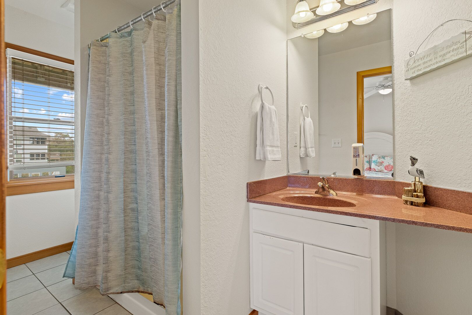 Un bany amb cortina de dutxa, un lavabo amb calaixera i un mirall amb llums.