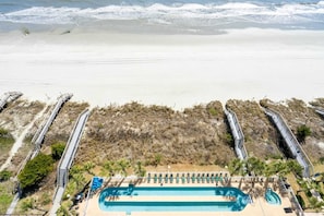 Un resort frente a la playa con una amplia piscina, tumbonas y una playa de arena.