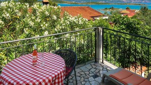 A balcony with a checkered table, a bottle of wine, and a view of a coastal landscape.