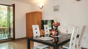 A dining area with a glass table, white chairs, a wooden cabinet, and a television.