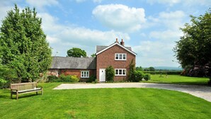 A brick house with a front lawn, a bench, and a pathway leading to the entrance. - Yew Tree Farm Cottage.. (Congleton)