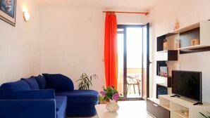 A living room with a blue sofa, a white coffee table, a TV on a white stand, and a red curtain. - Nice apartment for 4 guests with WIFI, A/C, TV, balcony and pets allowed (Novi Vinodolski)
