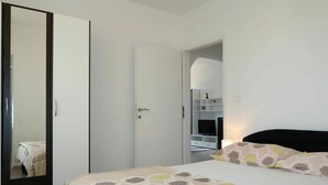 Une chambre à coucher avec un lit, une armoire et un téléviseur, le tout dans une pièce aux murs blancs.