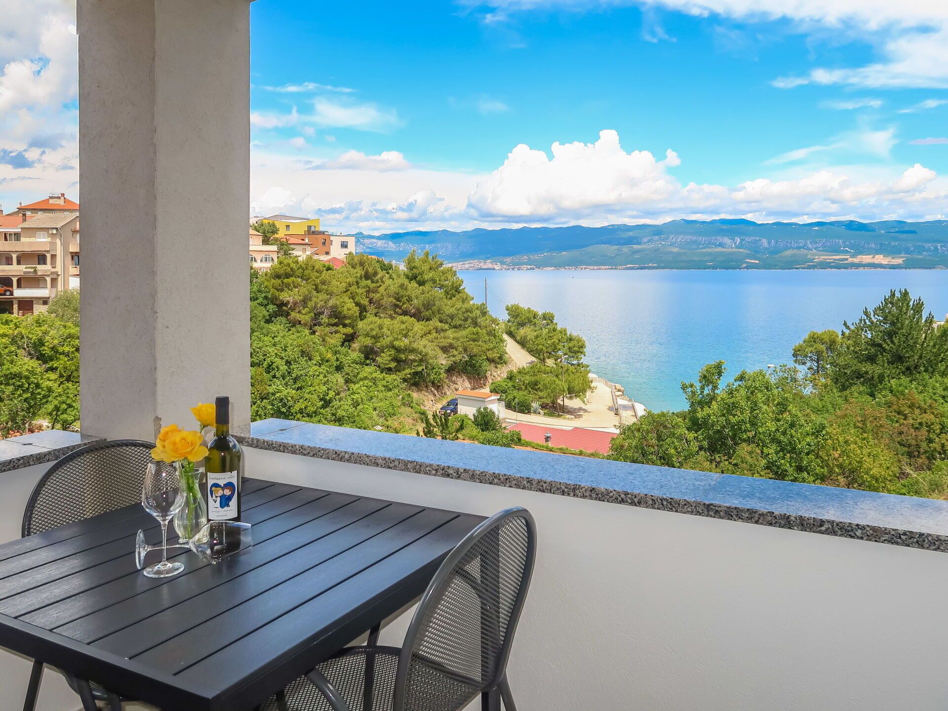 A balcony with a table and chairs overlooking a lake and mountains.