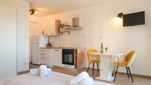 A compact hotel room with a bed, a small kitchenette, a dining area with a table and chairs, and a TV mounted on the wall.