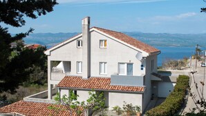 A two-story house with a tiled roof, a satellite dish, and a view of the sea.