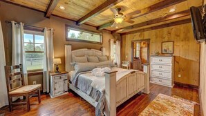 Un dormitorio con techo de madera, una cama, una silla, un tocador y una ventana.