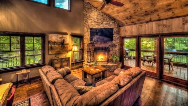 Una sala de estar acogedora con chimenea de piedra, sofá de cuero y ventanas amplias.