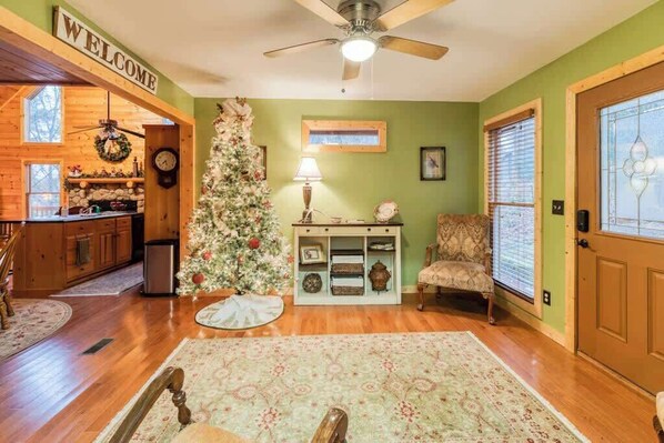 A cozy interior with a wooden floor, a Christmas tree, a 'WELCOME' sign, a chair, and a door with a window. - Cabin at Twin Creeks (Blue Ridge)