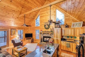 A log cabin interior with a fireplace, wooden cabinets, a television, and a dining area. - Cabin at Twin Creeks (Blue Ridge)