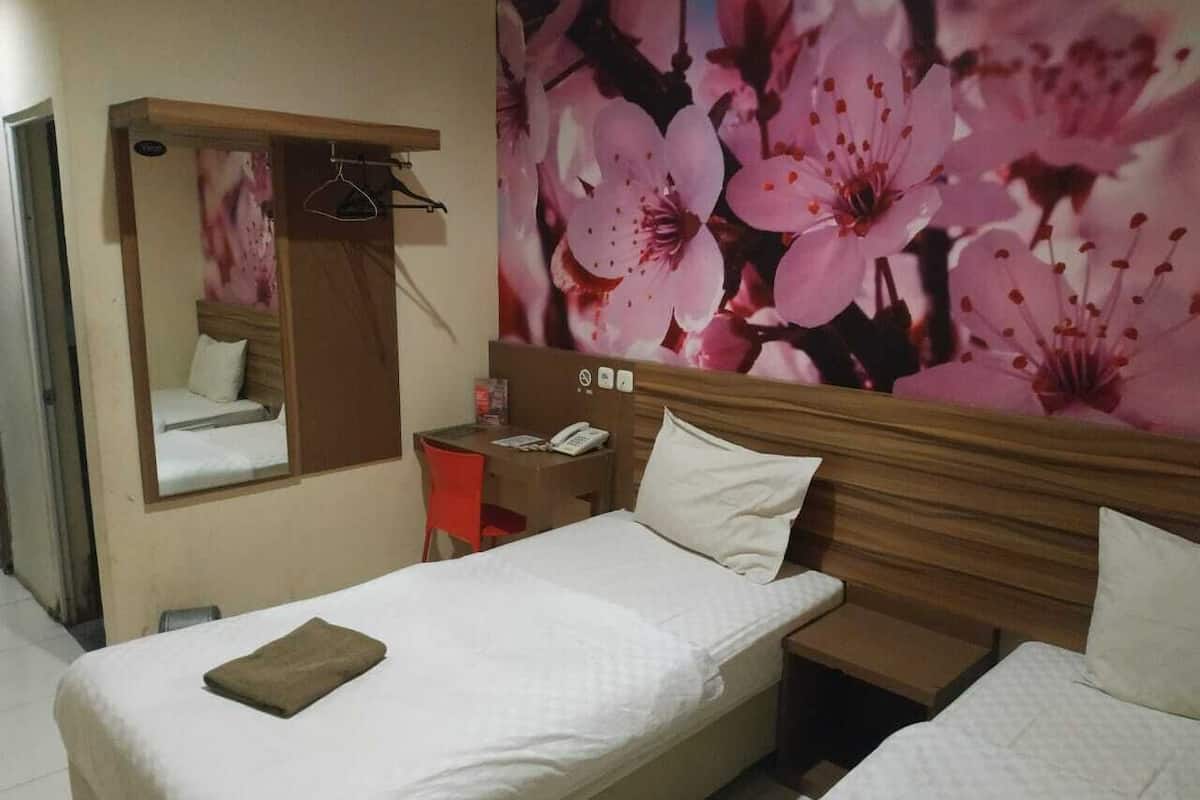 Una habitación de hotel con una cama individual, un escritorio con teléfono, una silla y un espejo.