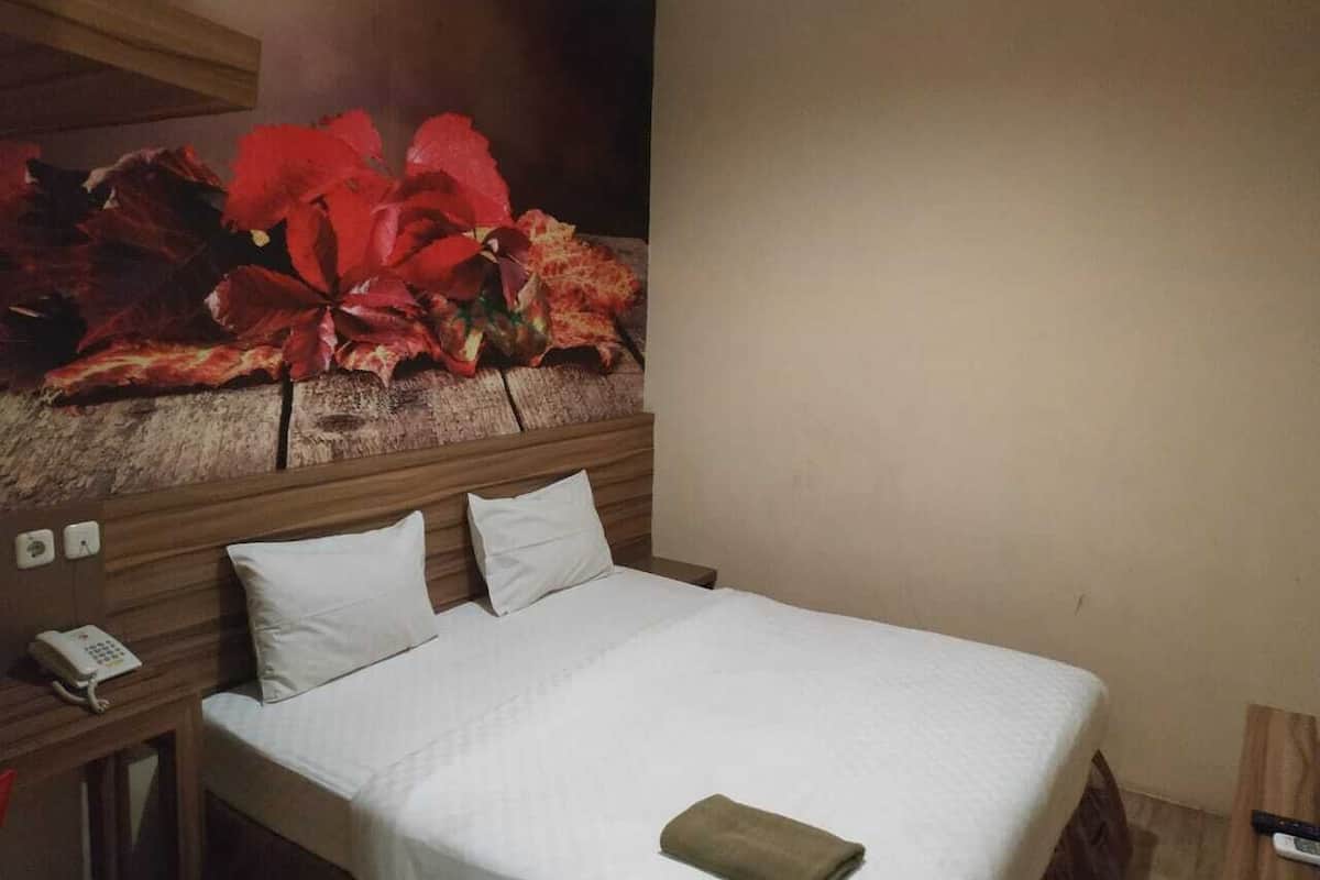 Habitación de hotel con cama, mesita de noche con teléfono y un cuadro grande con motivos florales en la pared.