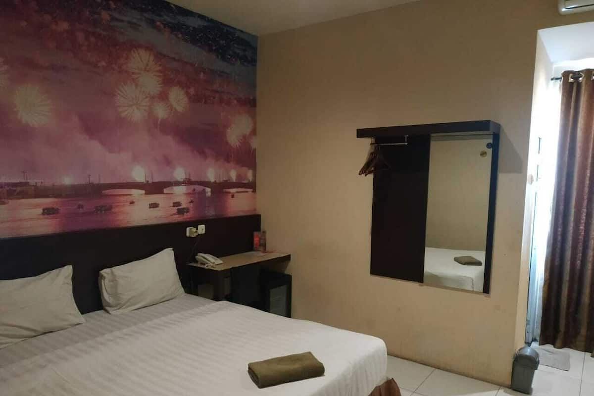 Una habitación de hotel con una cama, un escritorio, un espejo y una repisa en la pared.